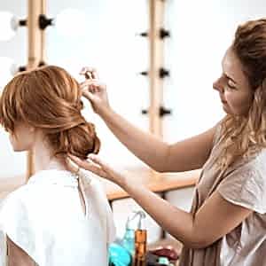Female hairdresser making hairstyle to beautiful redhead girl in beauty salon. Copy space.